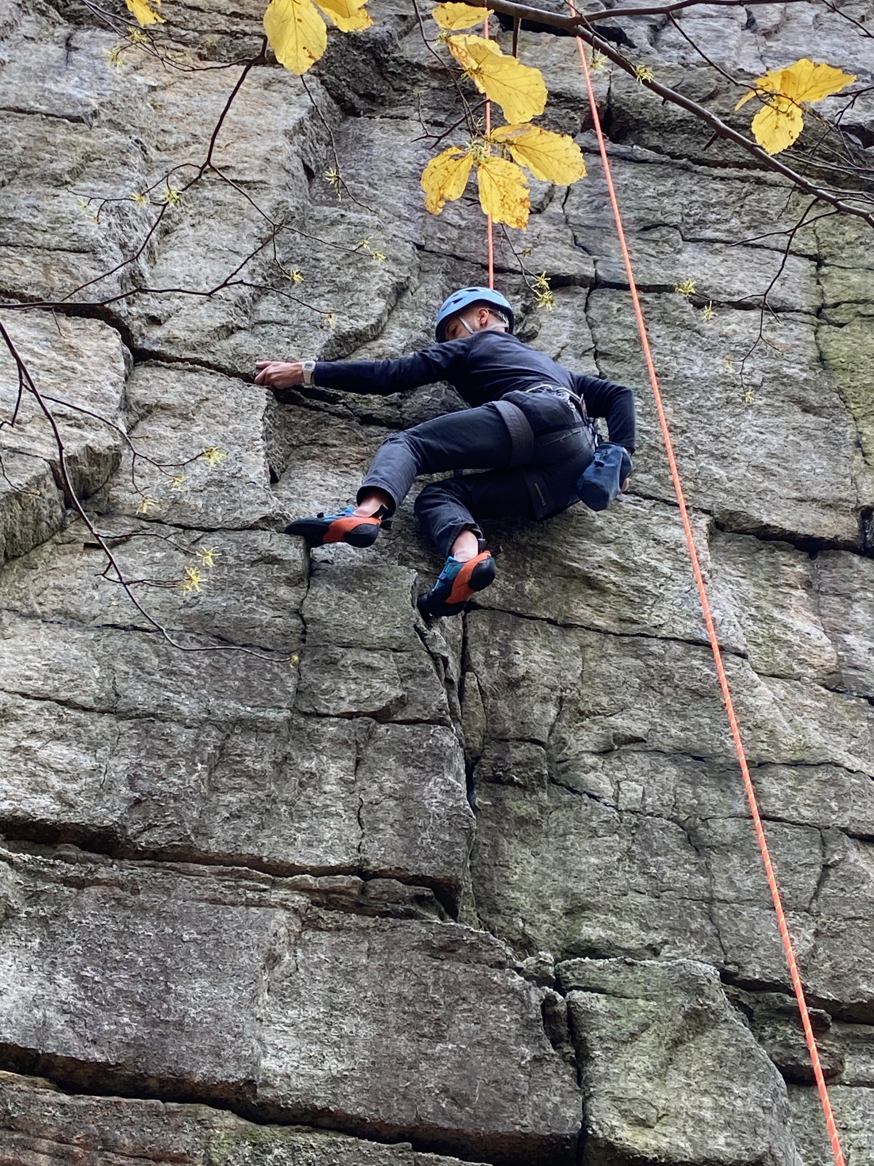 Me, climbing a flat rock wall with a rope going from my harness to the top of the cliff, then back down to the ground.