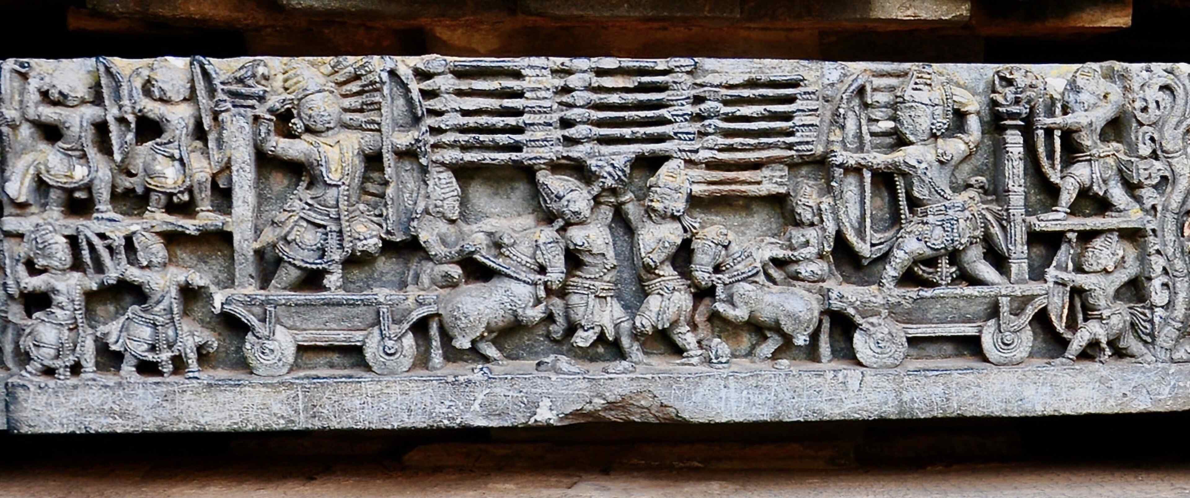 A damaged frieze sculpture of Arjuna on a chariot filling the air in front of him with arrows, so dense they are stacked five high and tip-to-tail in three layers, all aimed at Karna. They are surrounded by smaller soldier figures.