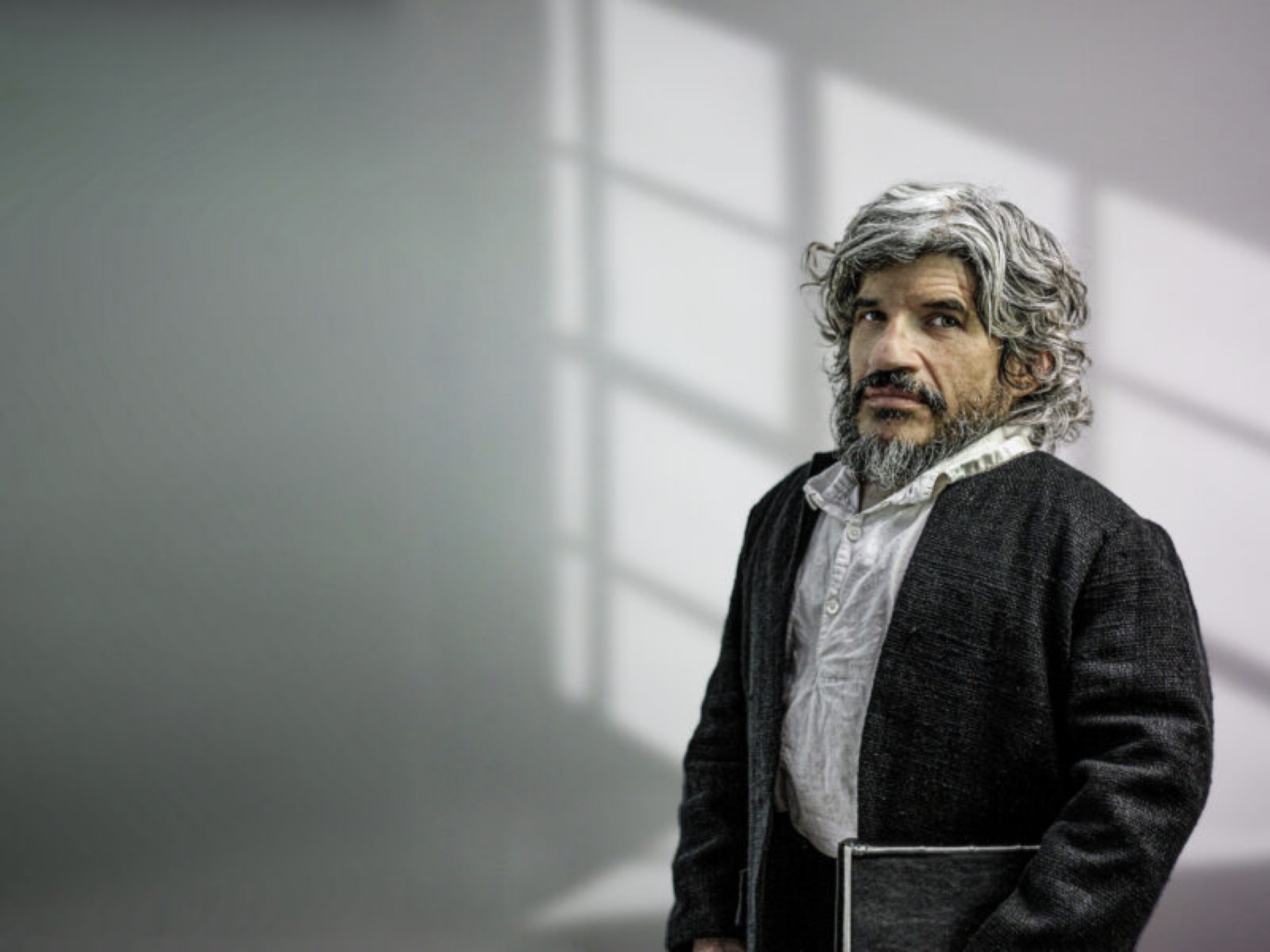 Photo of Mark Povinelli, in costume as Benjamin Lay, with a rough black jacket, holding a book.