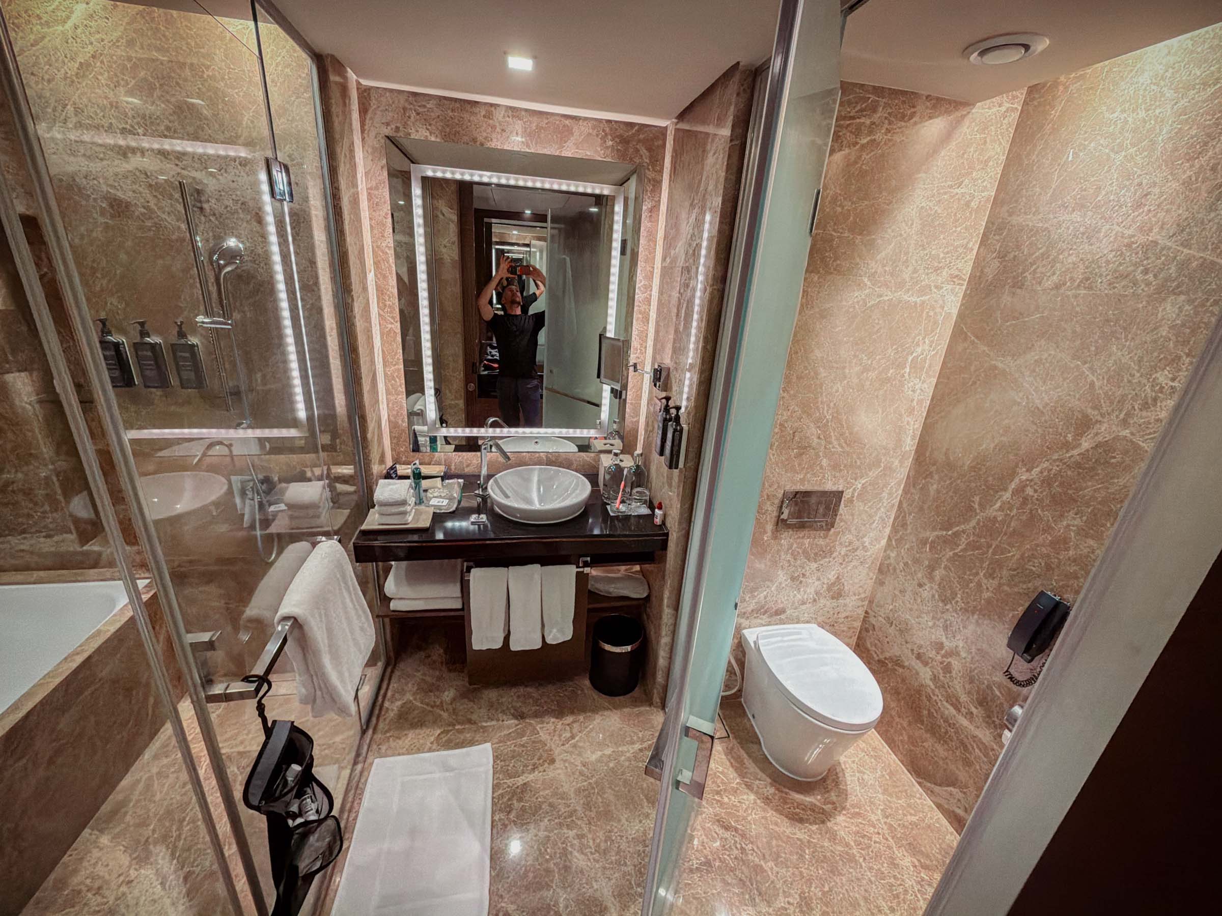 A hotel bathroom with marble floors and walls, a glass shower, and a bathtub