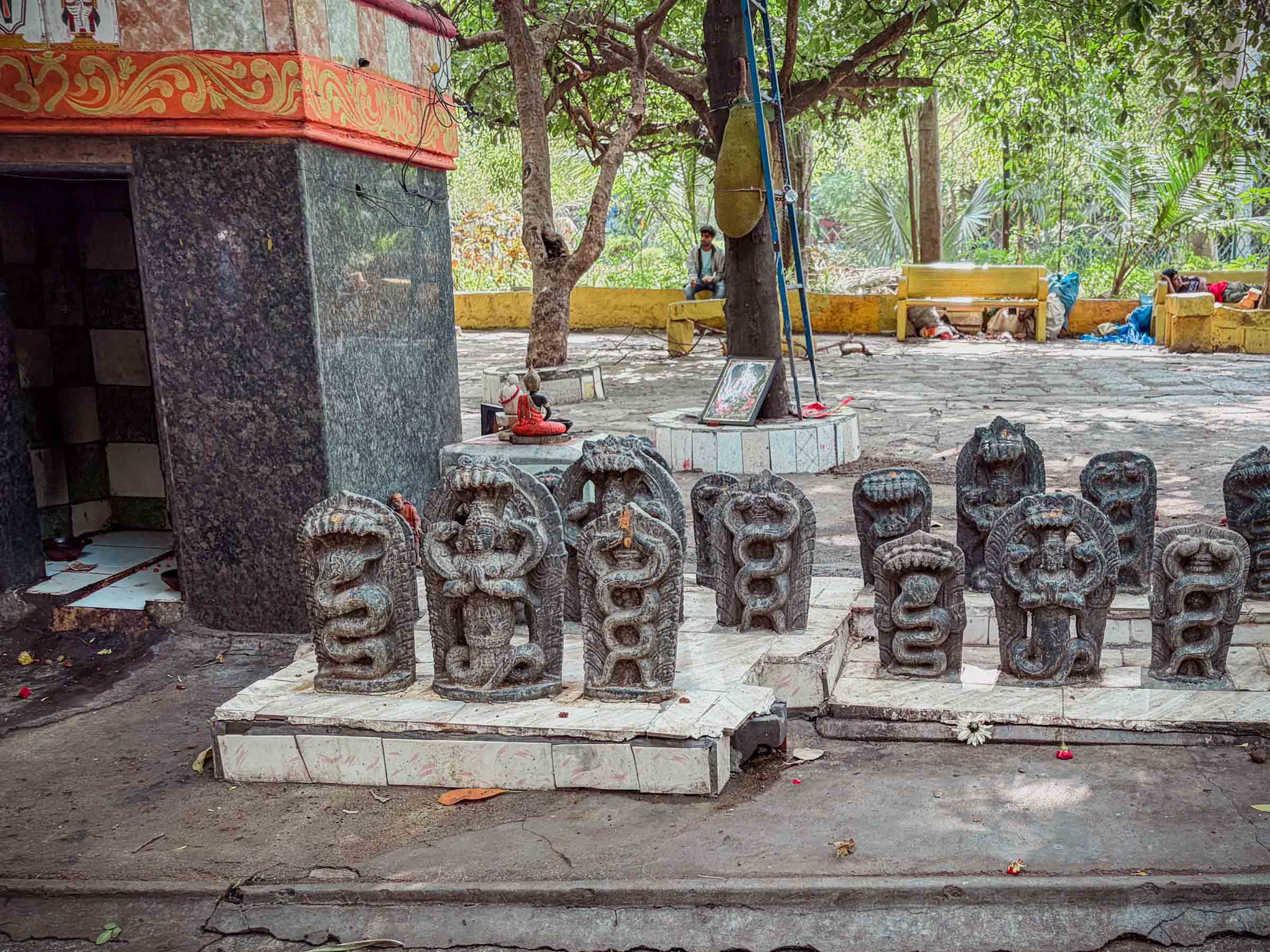 Rows of carved stone naga statues on a platform beside a small shrine