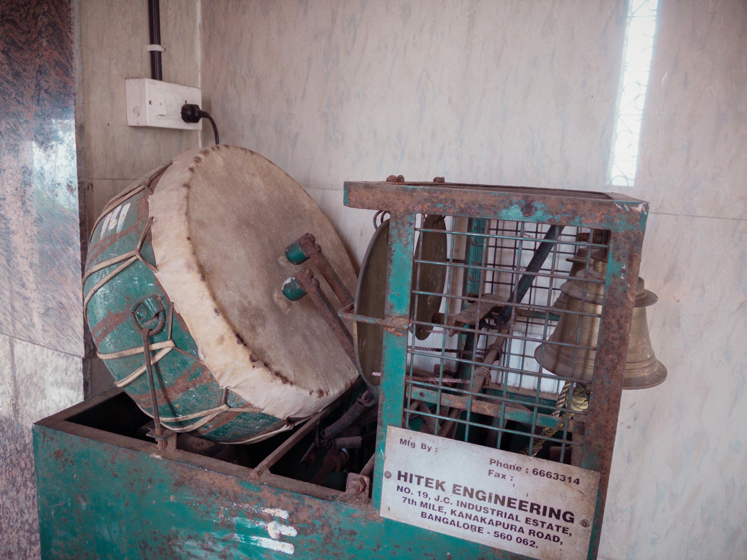 A green metal machine holding a ritual drum and a cage of brass bells