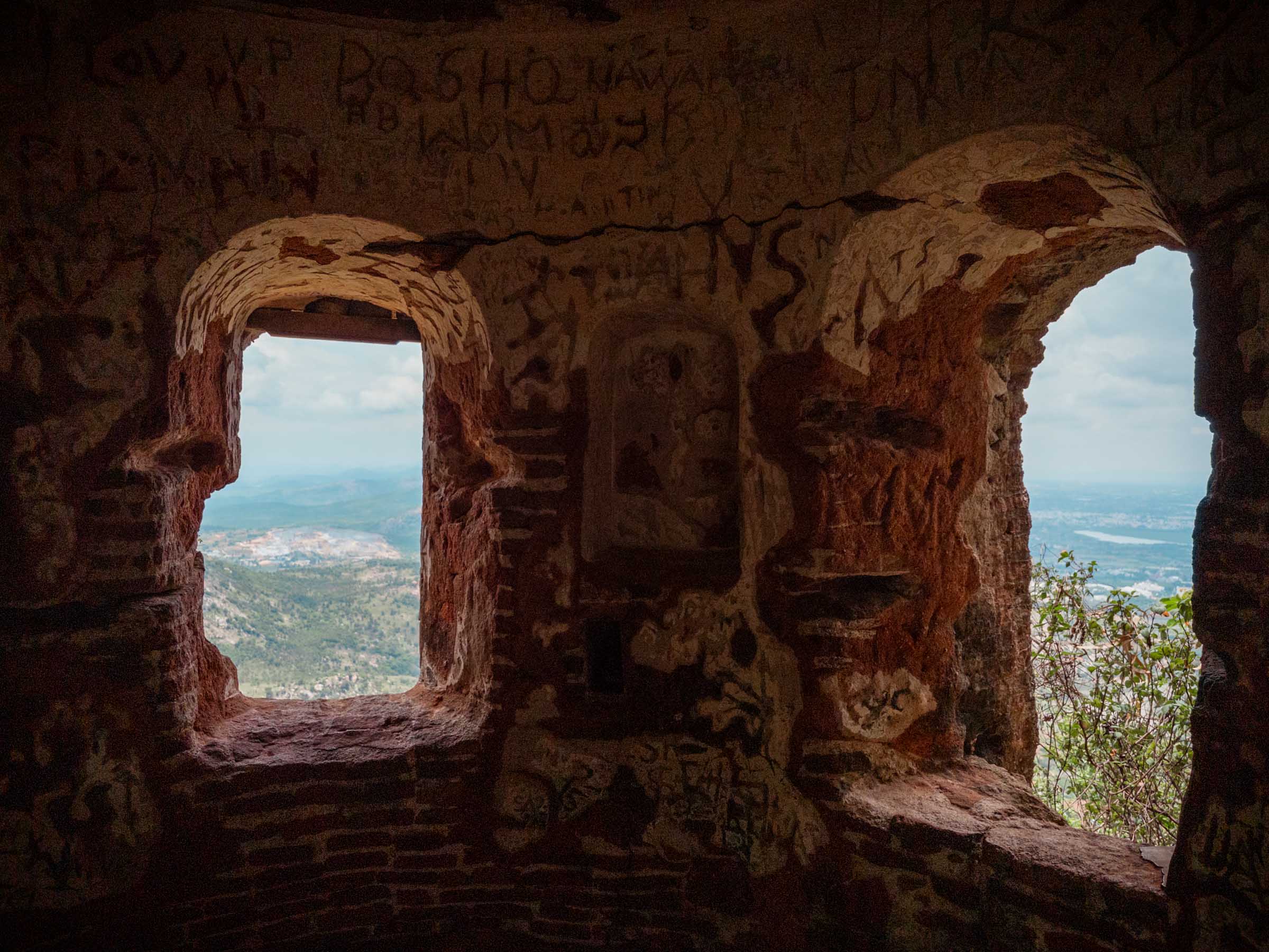 Interior of a ruined stone watchtower, its graffiti-covered arched windows framing the plains below