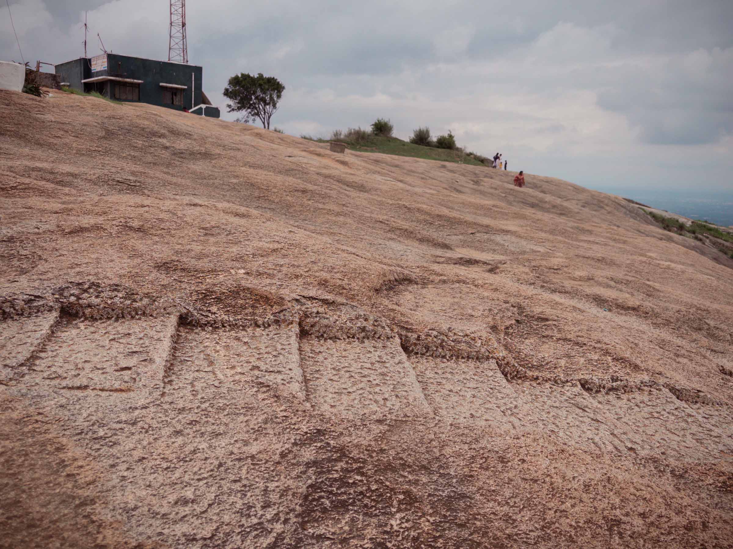 A yali, a mythical lion, carved into the smooth granite at the hilltop, with a temple beyond