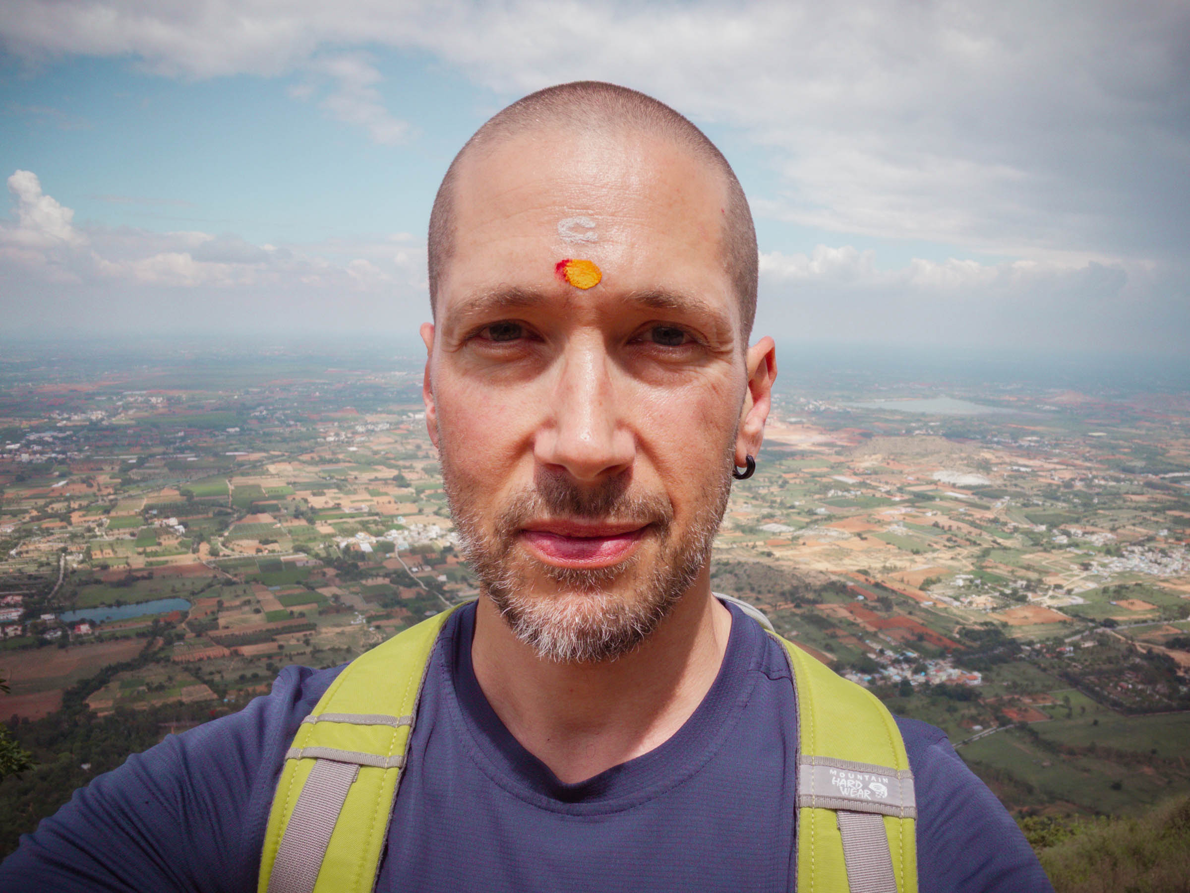 A selfie of me with red and yellow tilak marks on my forehead, the plains behind