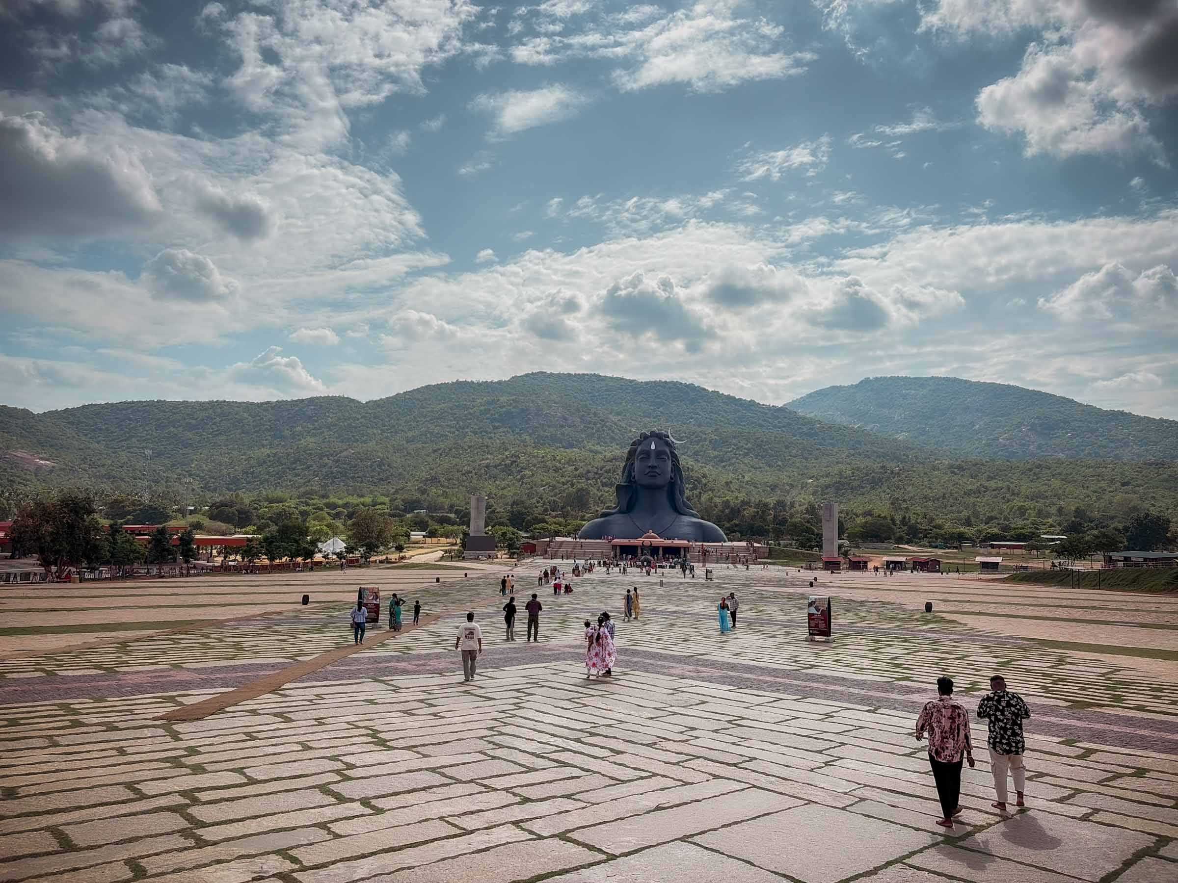 Visitors crossing a vast plaza toward the giant Adiyogi Shiva head in the distance
