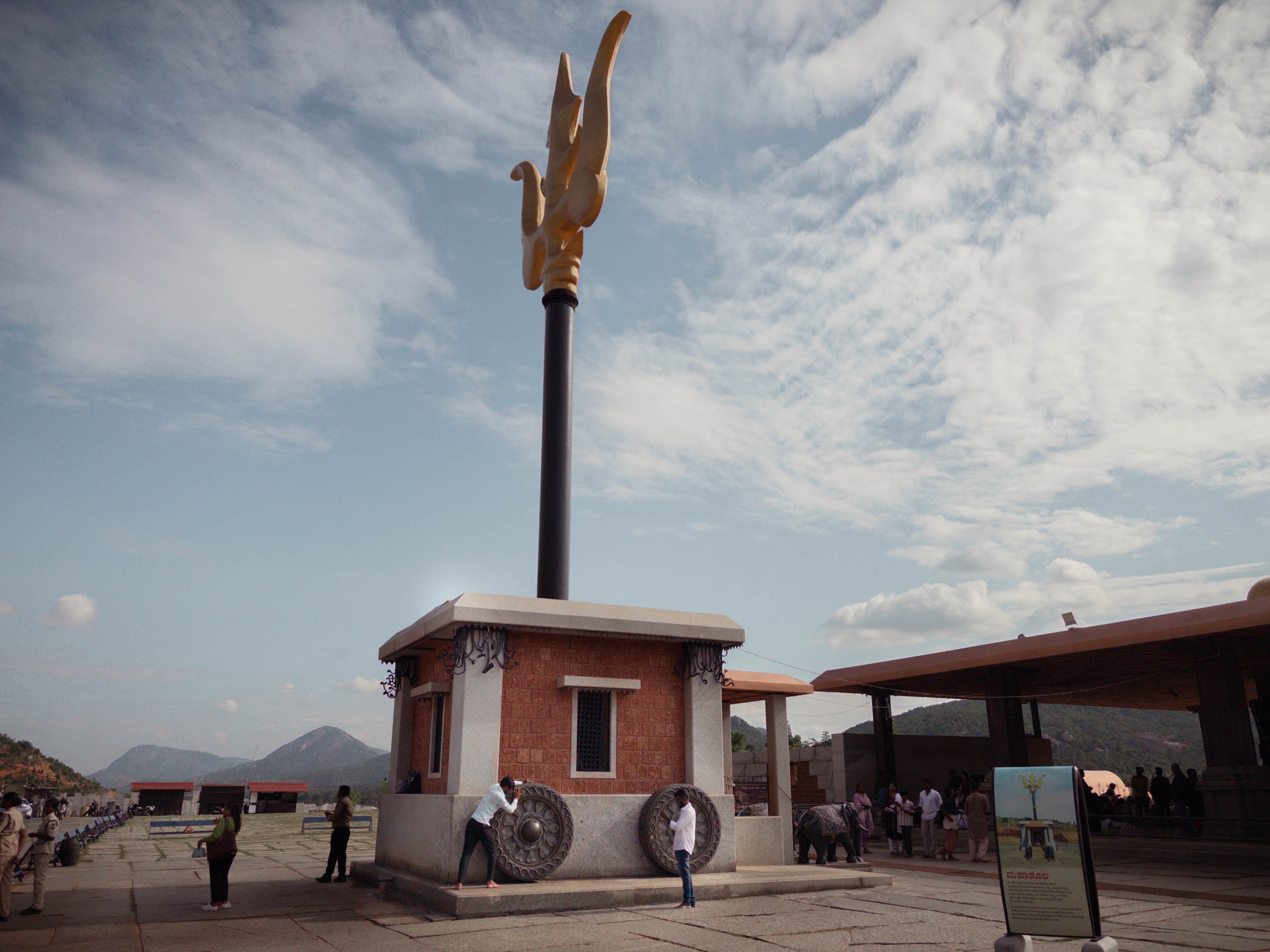 A lingam shrine shaped like a wheeled wagon, topped by a golden trident, its wheels turned by visitors