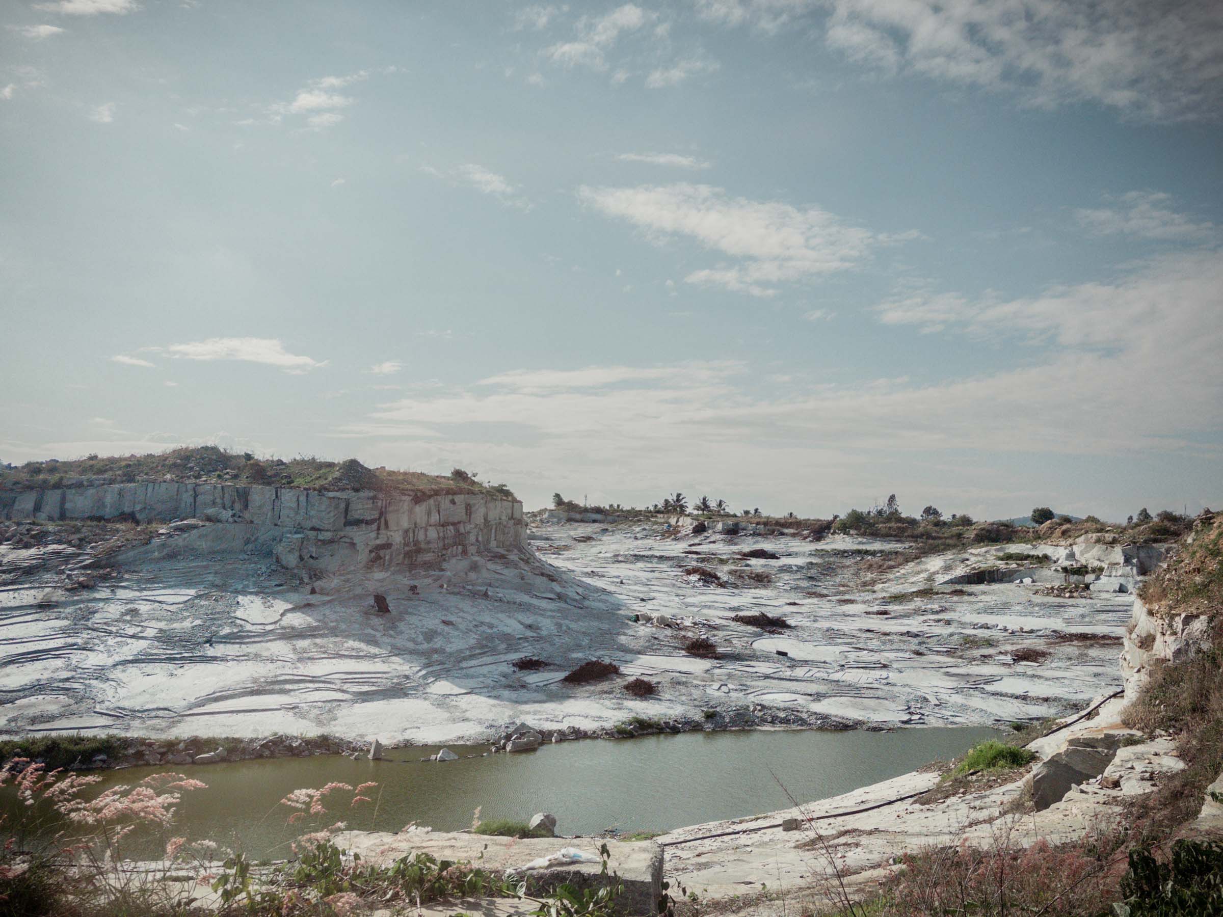A quarry of white stone with a green pond at its base, beside the road to Bangalore