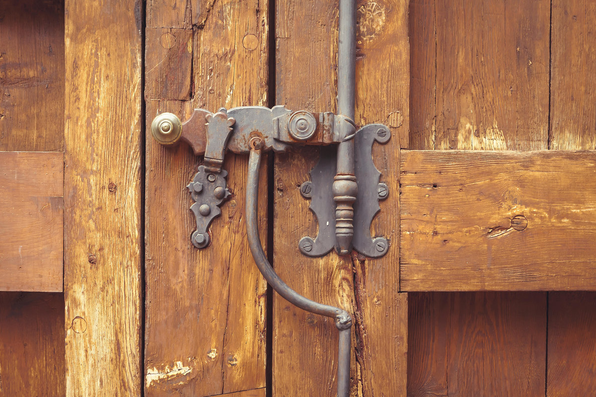 A wooden door secured by a very simple metal lock that appears some centuries old