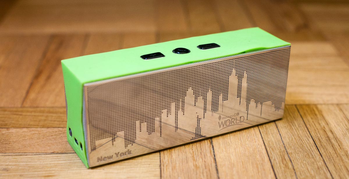 Green portable speaker with a New York City skyline stenciled into its shiny metal front panel. The panel has "New York MongoDB World" embossed in it.