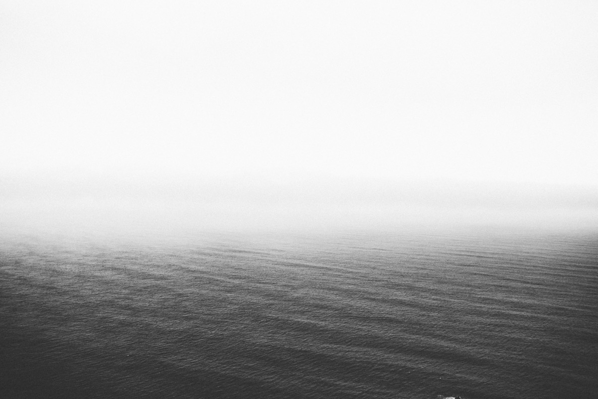 Image Description: grainy black-and-white image of calm ocean with misty sky fading to white at the top