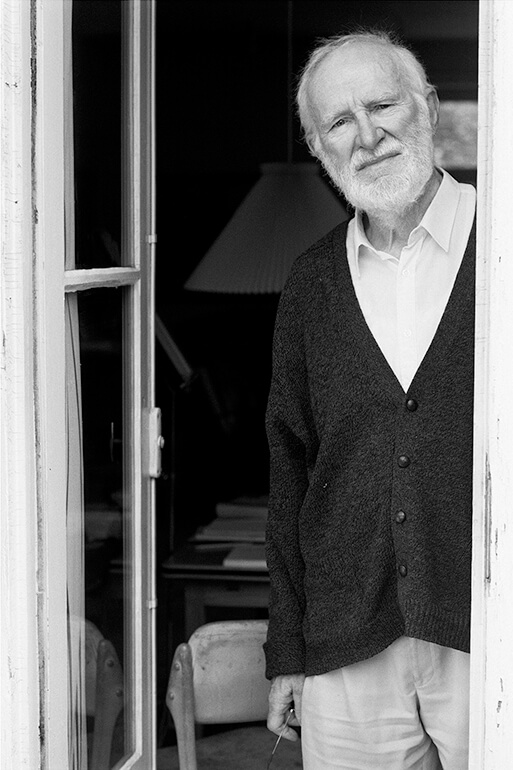 Black and white photo of Peter Naur, a white-haired man with a white beard and a serious expression, standing in a doorway.