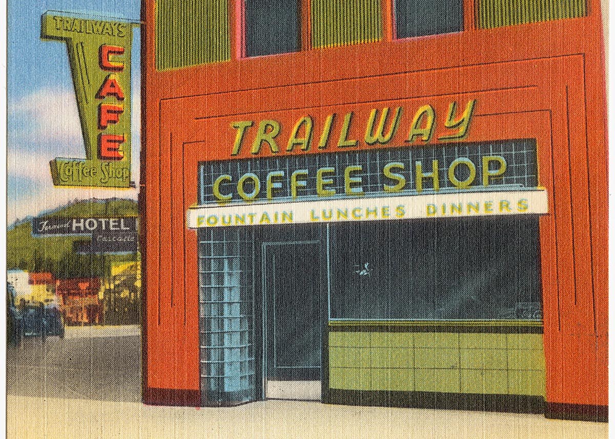 Description: 1930s postcard, drawing of old-fashioned roadside cafe. The sign says "Trailway Coffee Shop: Fountain Lunches Dinners." In the background is a forested hill with blue sky.