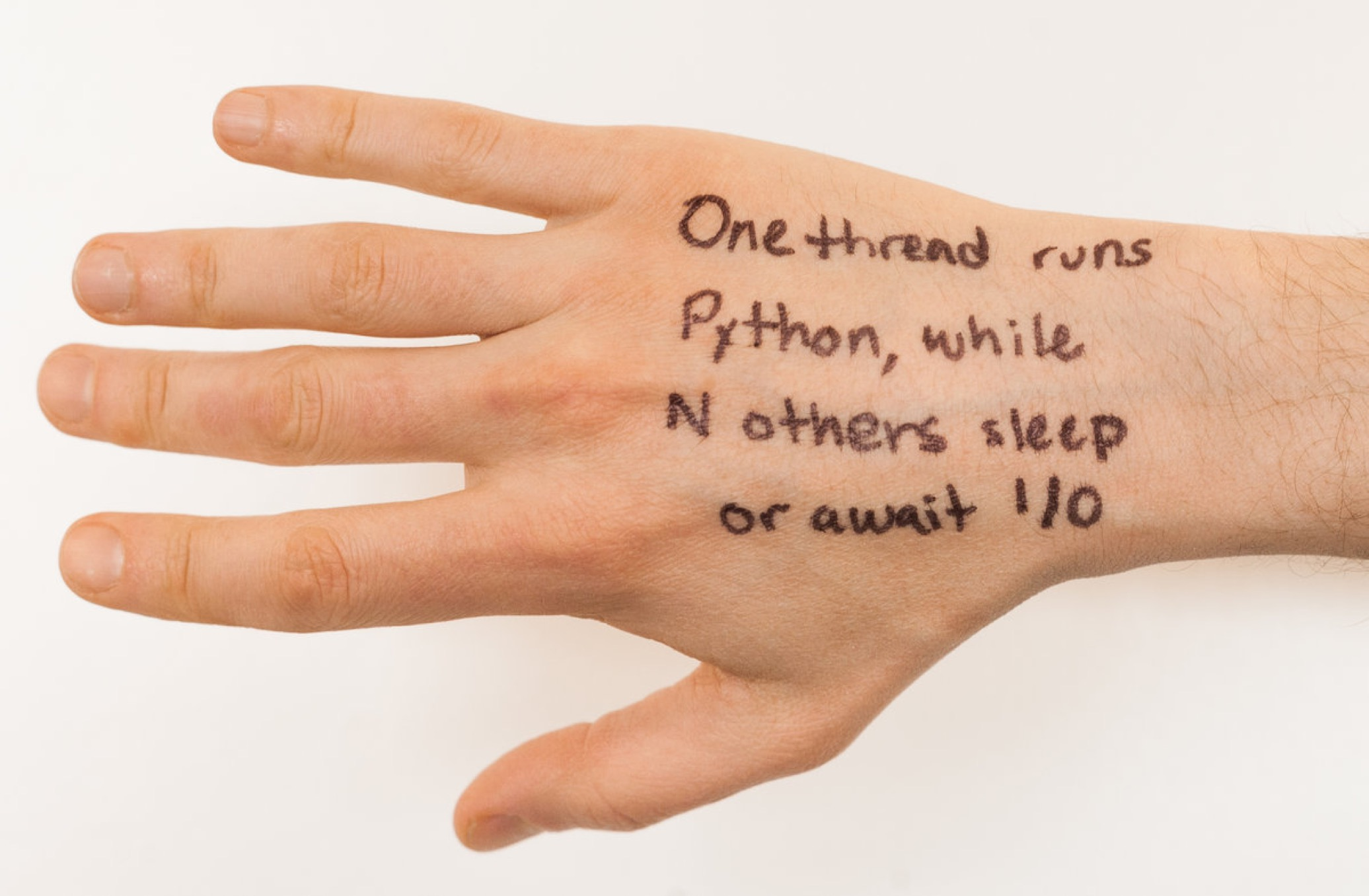 Photo of a hand with the following text written on its back: One thread runs Python, while N others sleep or await I/O.